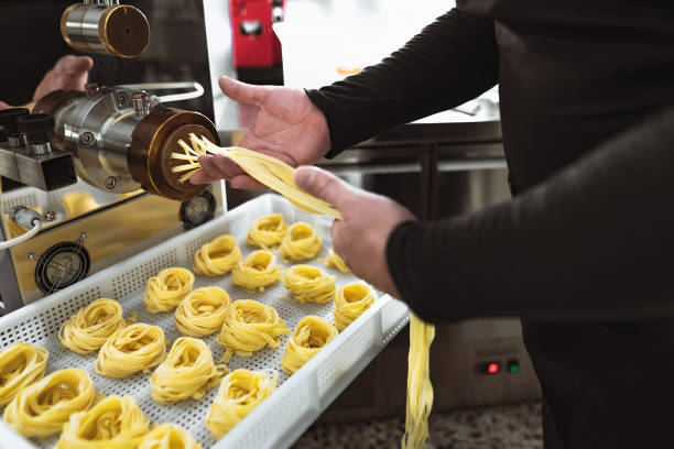 istock Close up male hands preparing fresh fettucine using machine inside pasta factory 1400882462