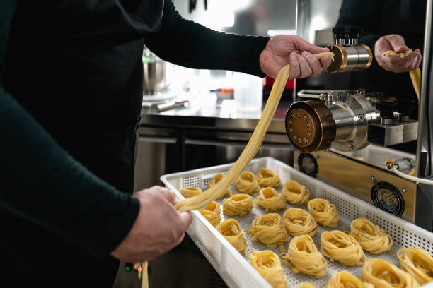 istock Close up male hands preparing fresh fettucine using machine inside pasta factory 1400882475