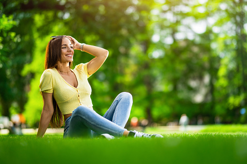 Beautiful young woman relaxing while sitting on grass in the park.