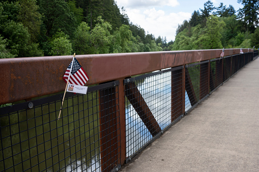 Tualatin, OR, USA - May 30, 2022: American flags with name cards honoring military personnels who fought and died in service are seen on a bridge over Tualatin River in Oregon on Memorial Day.