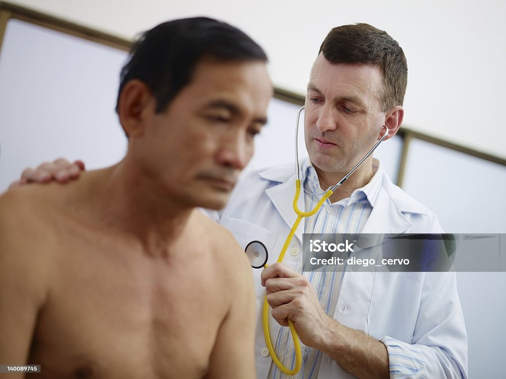 Doctor working and visiting old man in clinic caucasian doctor working and visiting old asian male patient in hospital with stethoscope Doctor Stock Photo