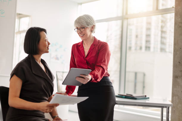 istock Two women talking face to face about ideas and plans using tablet computer in modern office daytime 1400927303