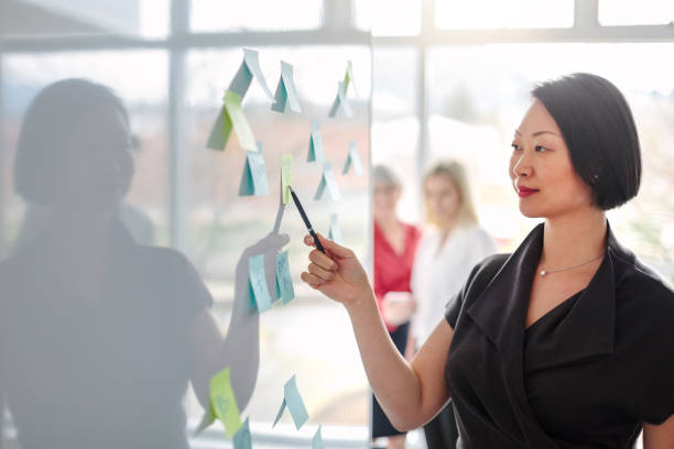 istock Korean mature woman reviewing ideas on notes on white board in modern creative office interior daytime 1400927360