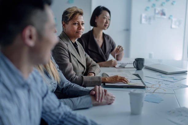 portret wielorasowej dojrzałej kobiety myślącej samotnie w samotności podczas spotkania z wielorasową grupą kolegów w kreatywnym wnętrzu biura - meeting community board room leadership zdjęcia i obrazy z banku zdjęć