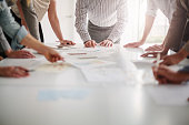 Low angle view of hands of multiracial group of people working with ideas and brainstorming together to make decisions with documents on table in creative office teamwork