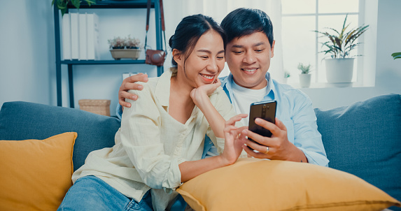 Young Asian married couple with casual sitting on couch use smartphone online shopping in living room at home.