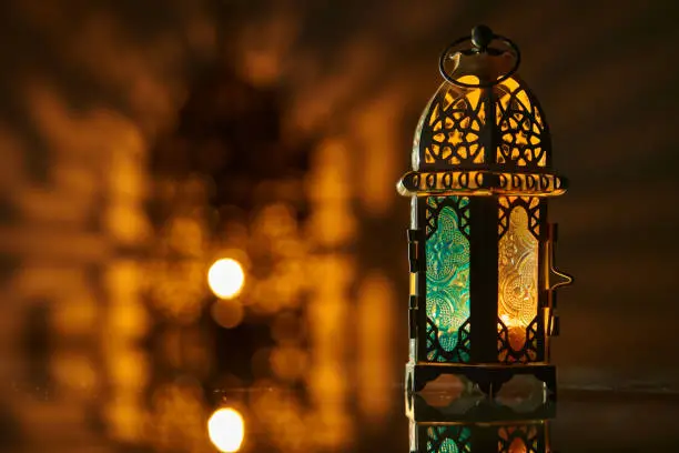 Ornamental Arabic lantern with burning candle glowing at night.