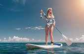 Woman sup sea. Happy healthy fit woman in bikini relaxing on a sup surfboard, floating on the clear turquoise sea water. Recreational Sports. Stand Up Paddle boarding. Summer fun, holidays travel