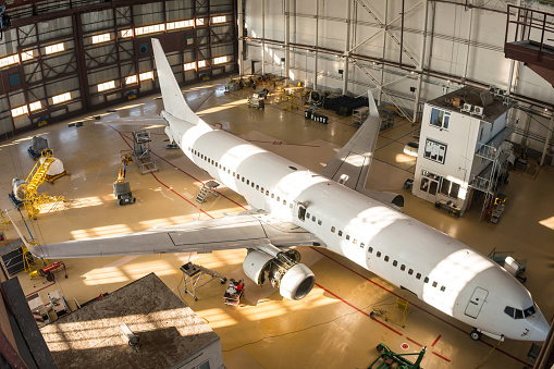 Top view of a white passenger airplane in the hangar. Aircraft under maintenance. Checking mechanical systems for flight operations