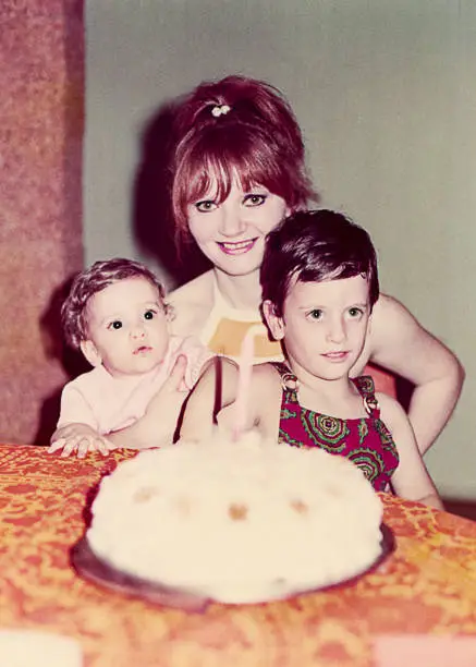 Vintage photo of a family celebrating the first year birthday of a little girl with mother and brother in front of the birthday cake.