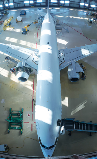 Top view of a white passenger jet plane in the hangar. Airplane under maintenance. Checking mechanical systems for flight operations