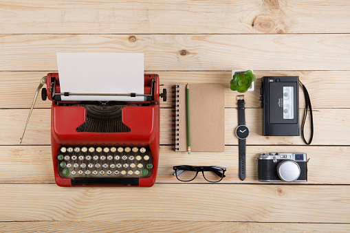 Writer or journalist workplace - vintage red typewriter, photo camera, cassette recorder on the wooden desk