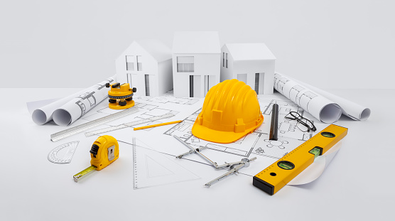 House construction plan concept. Tools for draw blueprint and building work. Architectural models houses, yellow hard hat, meter and spirit level  above blueprint with rulers, pencil and compass