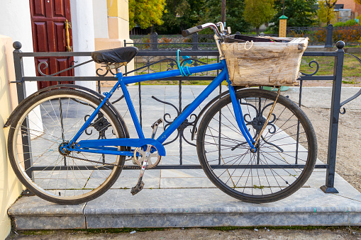 an old blue bicycle with a basket in front stands and a fence in front of the store. shopping on a bike