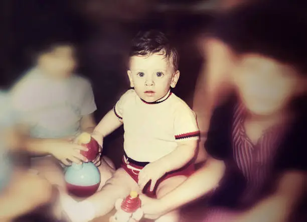 Vintage photo of a cute baby boy sitting on the floor and looking straight at the camera. Vintage photo of the seventies of the 20th century.