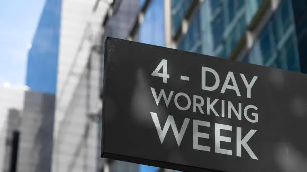 Photo of 4 - Day working week on a black city-center sign in front of a modern office building