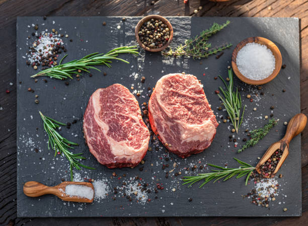 istock Raw Ribeye steaks with salt and herbs on grey board. Top view. 1400957364