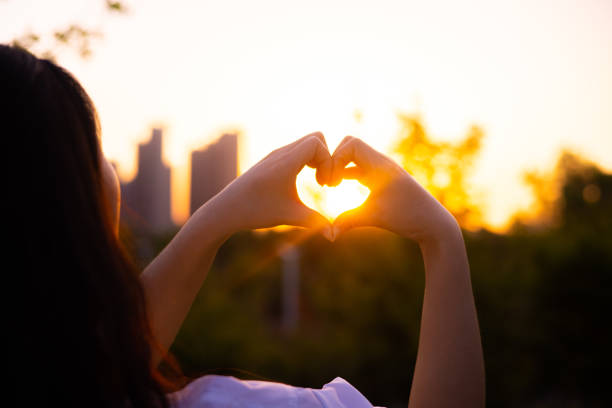 women hands making heart shape against the sunset