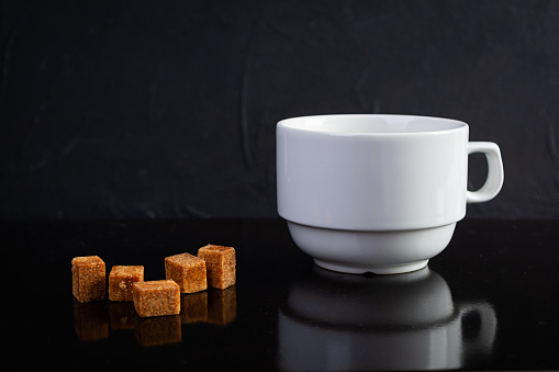 Cup of coffee with sugar and coffee beans on dark background