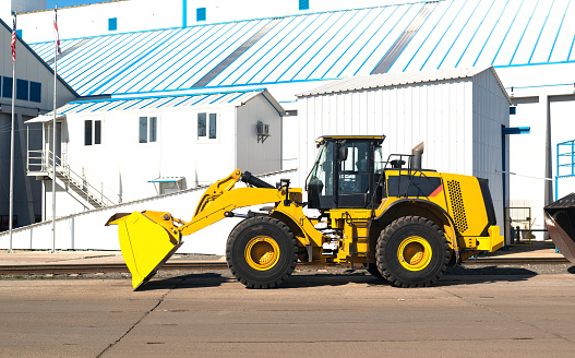 a bulldozer or tractor with a bucket of industrial machinery parked on a construction site or warehouse.