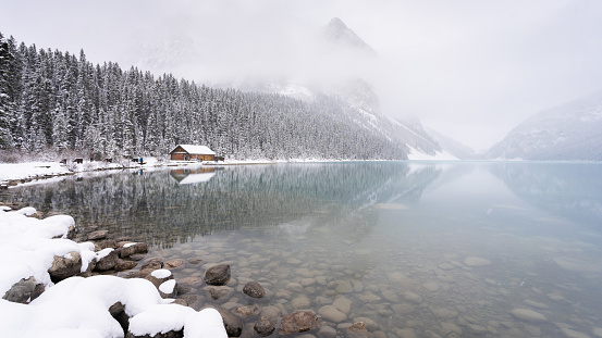 Almost frozen azure alpine lake shrouded by fog in early winter, Banff N. Park, Canada