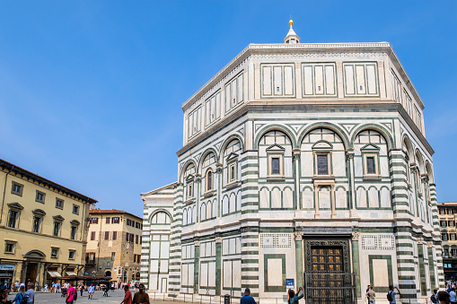 The octagonal Baptistery of Saint John in Florence, completed in the 12th century, together with the Cathedral and the Giotto's Campanile, is part of the UNESCO World Heritage Site. Tourists strolling in the square.