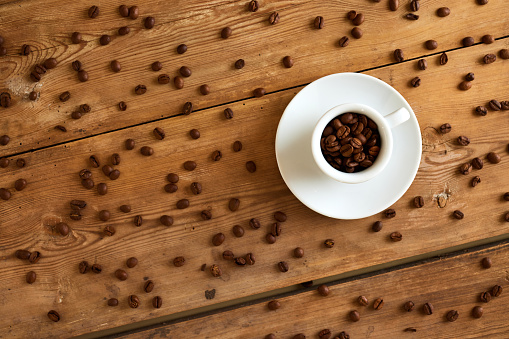 Overhead view of coffee beans in cup with spilled seeds scattered on wooden table with seamless pattern