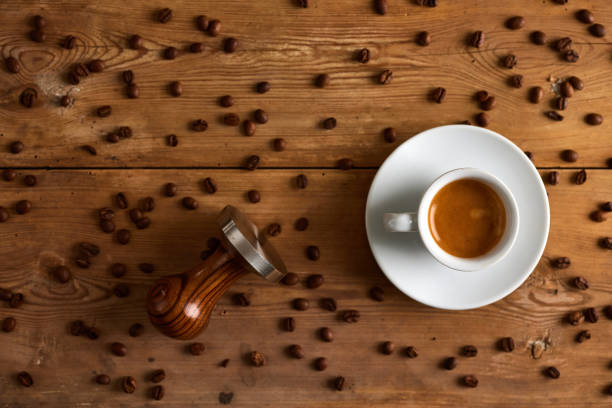 Coffee beans in cup with spilled seeds and tamper on table