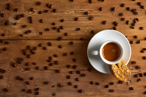 Coffee beans in cup with spilled seeds and cookie in saucer on table