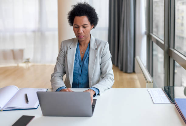 istock Serious businesswoman using laptop while sitting by window at desk in office 1400967294