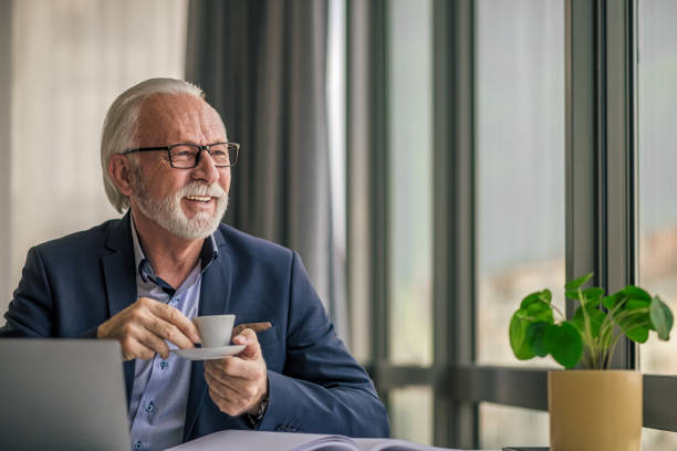 istock Smiling senior businessman having coffee while looking through window at office 1400967330