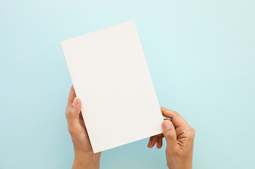 Cropped Hands of Man Holding Blank Book Against Blue Background