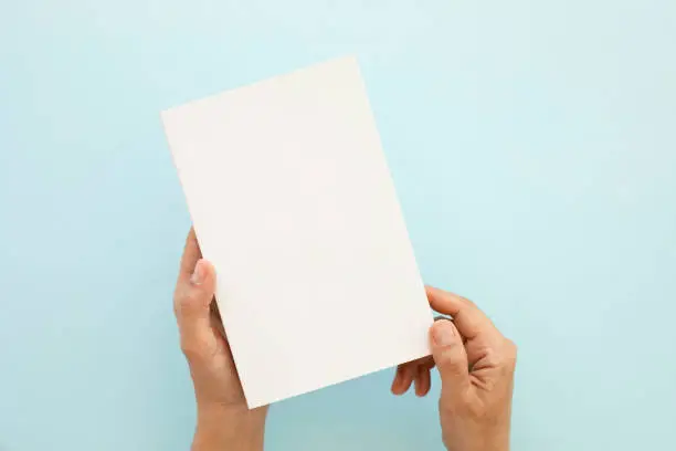 Photo of Cropped Hands of Man Holding Blank Book Against Blue Background