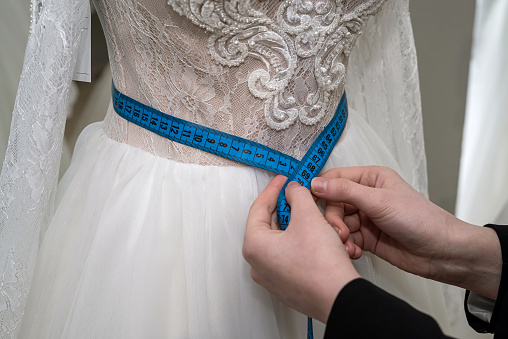 female consultant in a store measures a wedding dress with measuring tape