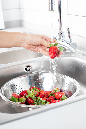 Woman is washing strawberry in the kitchen.