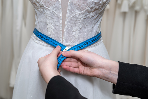 close up of female designer hand fitting bridal dress with measure tape in  boutique