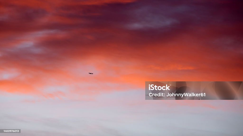 Airplane against red morning clouds Distant small Airplane seen against red morning clouds over Andalusian village Airplane Stock Photo