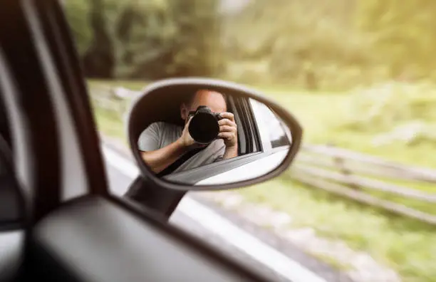 Photo of man takes photo in mirror in car. A man is taking photo someone or something from an open car window. Reflection in the side mirror of the car