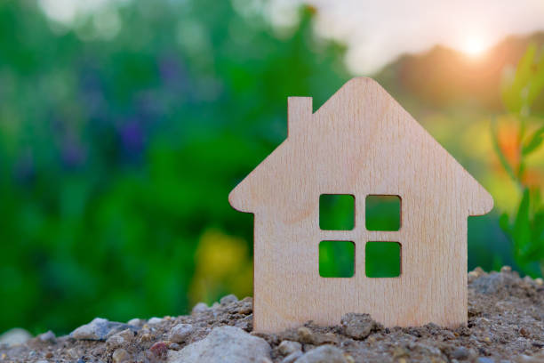 a small toy wooden house stands on the ground against the backdrop of green foliage and sunlight.The idea is real estate in an ecologically clean area, ecology and nature, a favorable life for people una pequeña casa de madera de juguete se encuentra en el suelo contra el telón de fondo del follaje verde y la luz del sol. la idea es inmobiliaria en un área ecológicamente limpia, ecología y naturaleza, una vida favorable para las personas