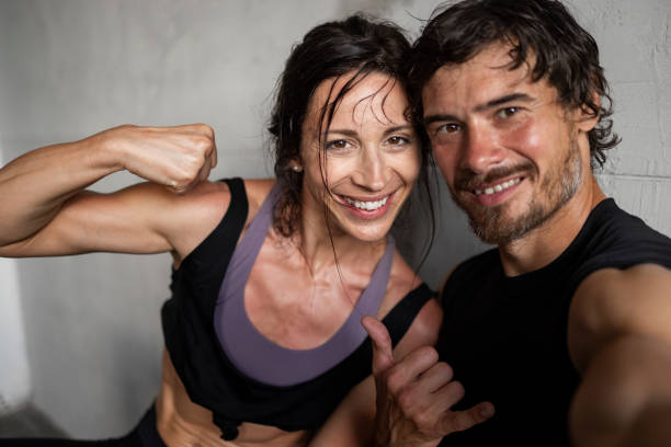 Portrait of a happy young muscular couple sitting in the gym together, finishing their training and taking a break after pushing themselves to their limit, looking at the camera