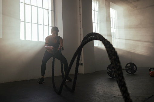 Fit muscular woman pushing herself in the gym, training with the ropes in a squatting position
