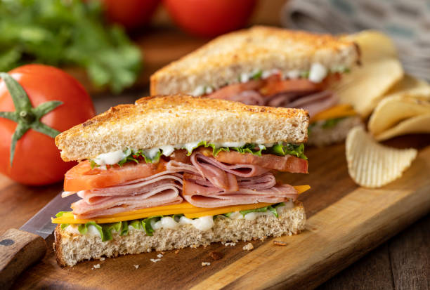 Ham sandwich with cheese, lettuce and tomato Ham sandwich with cheese, lettuce and tomato on whole grain bread.  Lettuce and tomatoes in background toasted sandwich stock pictures, royalty-free photos & images