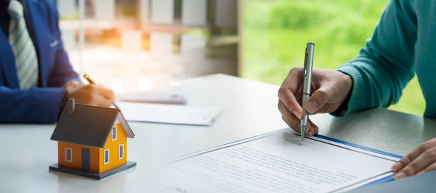 Real estate concept Young woman holding a pen signing a house purchase contract with a home sales representative in the office. stock photo