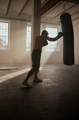Handsome muscular man training in the gym, using a punching bag for his boxing training and pushing himself to his limit