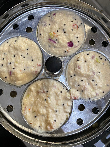 Stock photo showing close-up, elevated view of Rava idli (semolina) batter in a stainless steel mould ready to be cooked by steaming.