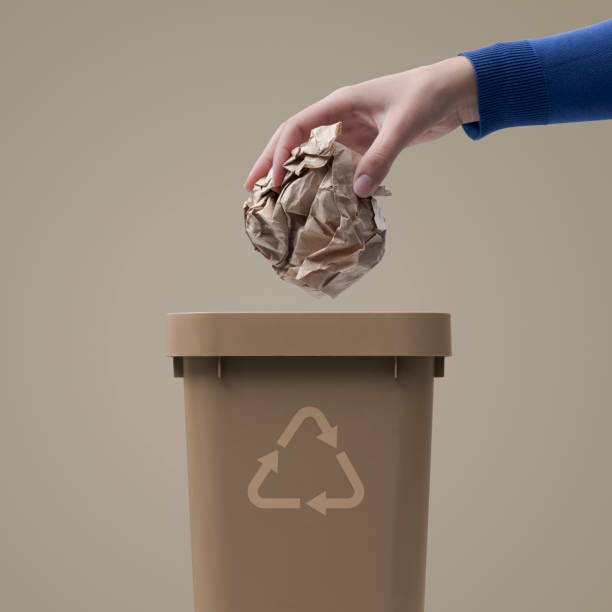 Woman putting crumpled paper in a trash bin, recycling and waste sorting concept