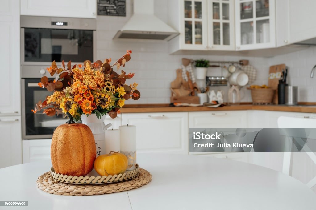 Still-life. Yellow, orange flowers in a vase, pumpkins and candles on a golden tray on a white table in a home kitchen interior. A cozy autumn concept. The concept of autumn, home comfort, hot drinks and warmth. Autumn Stock Photo