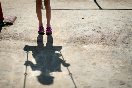 Feet and shadows of a child playing with a swing