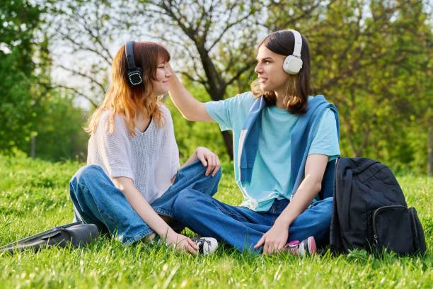 友人のカップル 17歳、18歳の男の子と女��の子 芝生の上に座っている - 18 19 years audio ストックフォトと画像