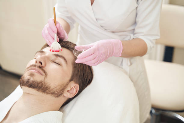 istock Cosmetologist applying peeling gel on man face with brush 1400996749